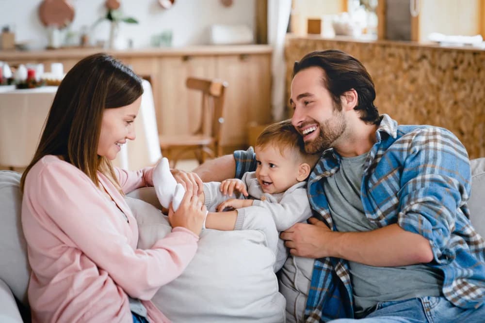 evde kanapede oturup, çocuğuyla oyun oynayan mutlu anne ve baba