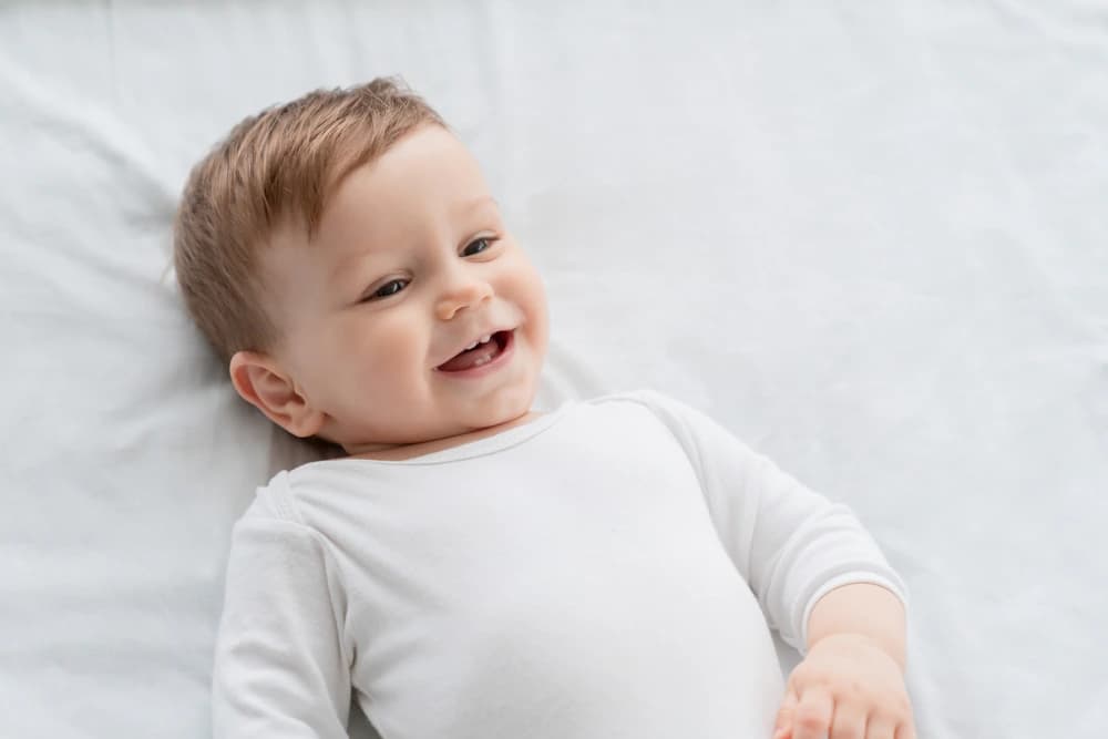 İlk dişleri görünen gülümseyen bebek yatağın üzerinde uzanıyor