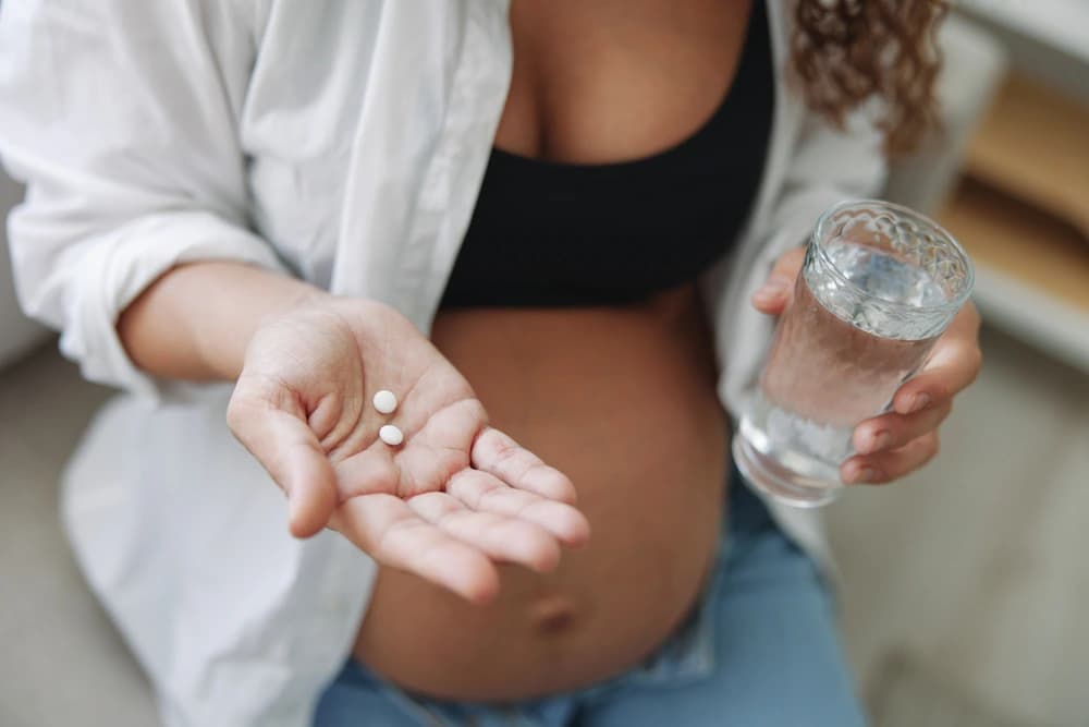 Hamilelikte D vitamini ne zaman başlanmalı konusu için elinde takviye hap ve su bardağı tutan hamile kadın