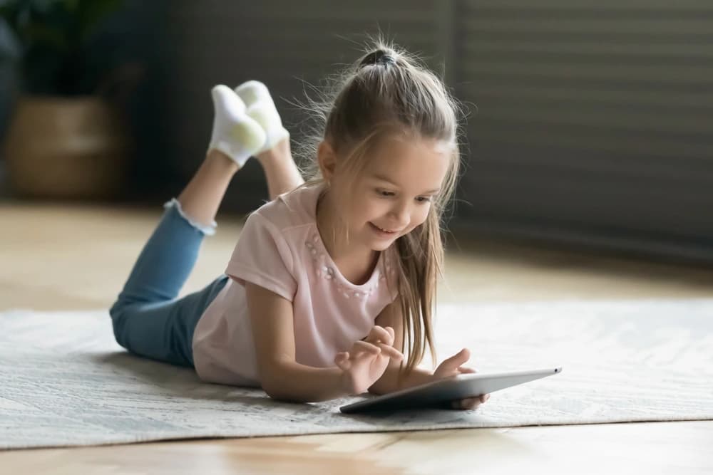 Yerde uzanarak tablete bakan küçük çocuk, çocuklarda ekran süresi konusunu yansıtıyor